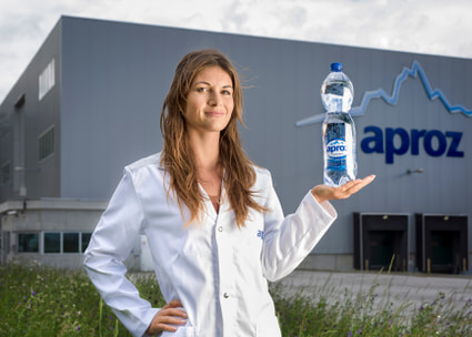 Junge Mitarbeiterin mit Wasserflasche vor dem Fabrikgebäude Thumbnail